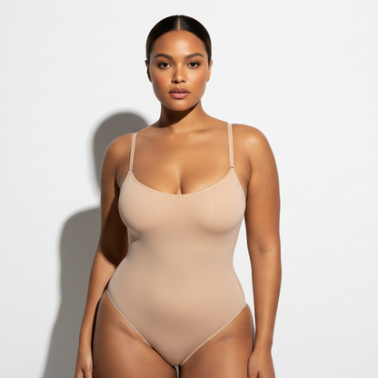 Professional 1:1 studiofoto van dezelfde vrouw. Geen verandering in gezicht of lichaam. Natural skin texture. Real pores. Dunne schouderbandjes. naadloos Shapewear bodysuit in nude. White studio. Zachte schaduw. Luxe fashion vibe. Sexy POSE. Direct eye contact. Warme bruine huid. Low bun. 26 jaar. Curvy bouw. Real skin.